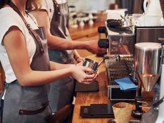 Baristas at an espresso machine steaming milk beside cups, City Service Index supports local cafes and small businesses